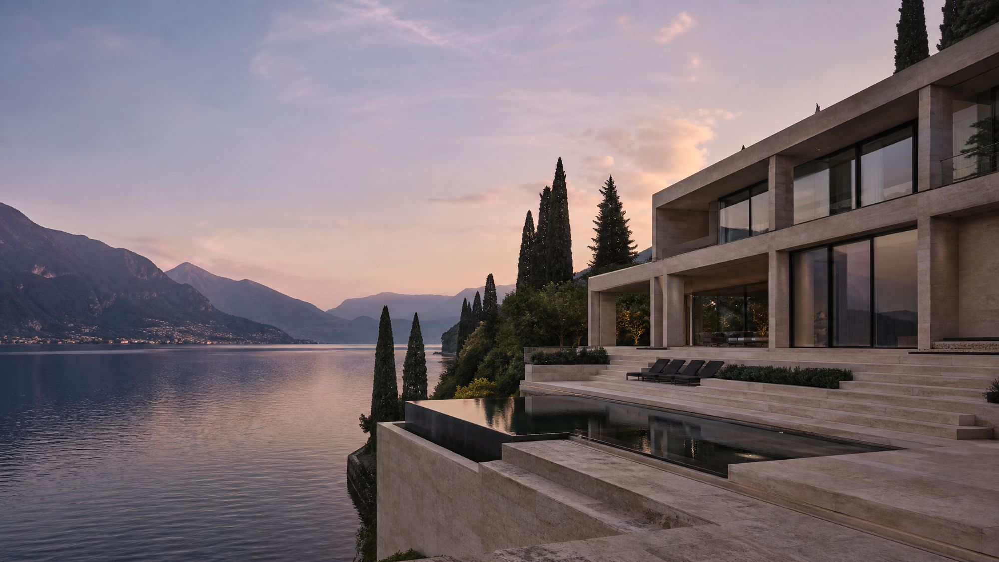 Pale limestone lakeside villa with an infinity pool above still water at dusk, Lake Como