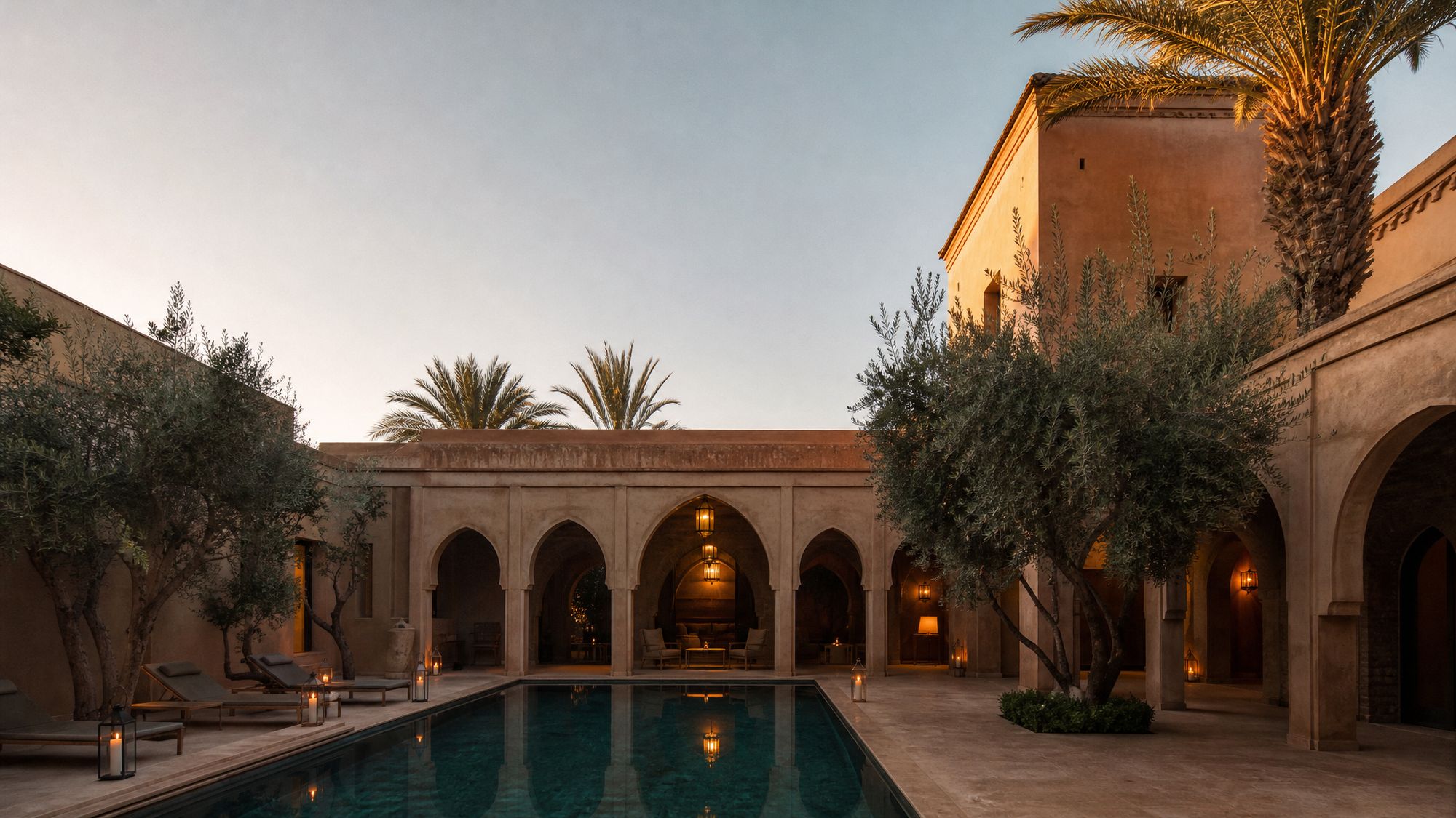 Ochre courtyard house with a long pool, olive trees and a lantern-lit arcade at dusk, Marrakech